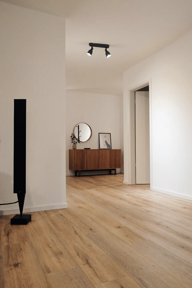 Freshly painted hallway with light walls, wood floors and a round mirror